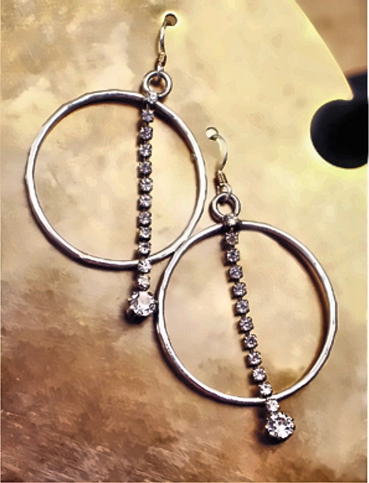 A pair of thin silver hoop earrings, each crossed by a hanging line of small rhinestones ending in a larger stone, on a brass ground.