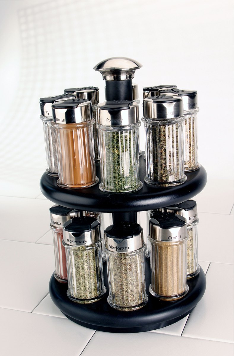 A black two-tier round spice carousel holding labeled cylindrical glass jars of herbs and spices with stainless steel lids.