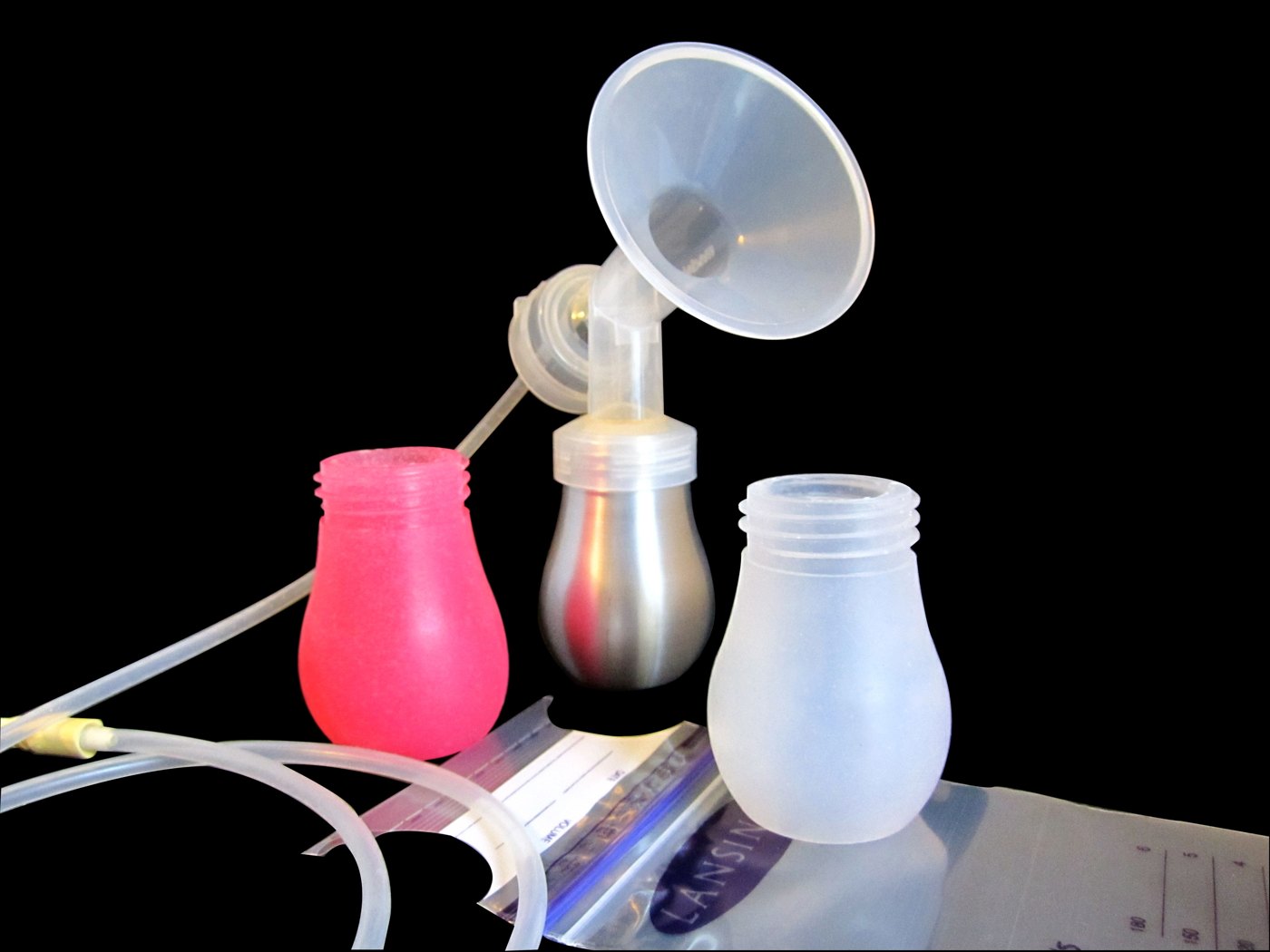 A breast pump flange on a stainless steel collection bottle, between a pink and a frosted clear bottle, with tubing and a storage bag, on black.
